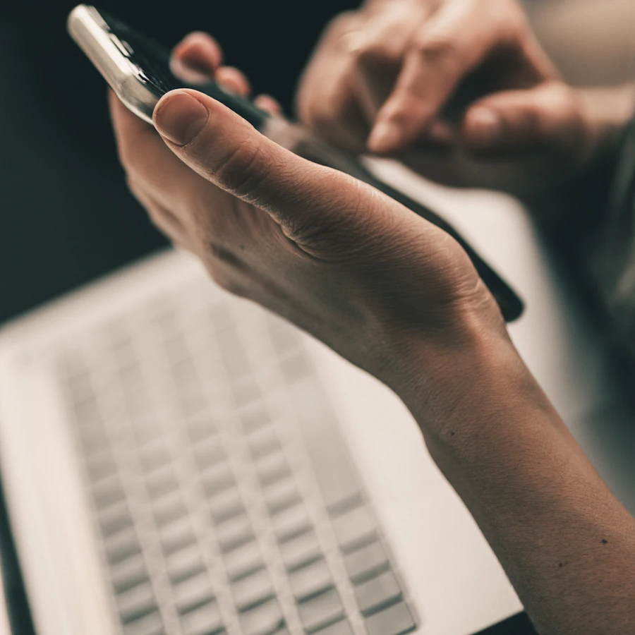 Someone using a phone above a laptop keyboard